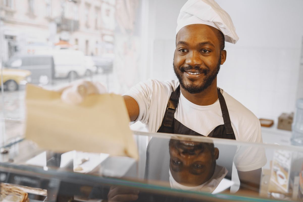 Fornaio sorridente che porge un sacchetto al cliente dal banco